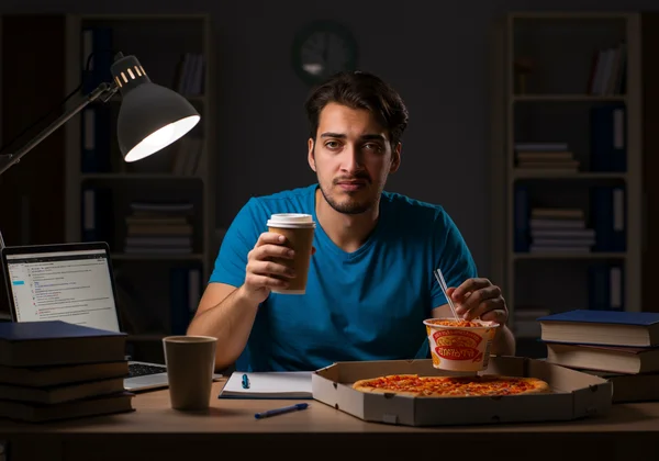 College student looking tired, surrounded by study notes and pizza
